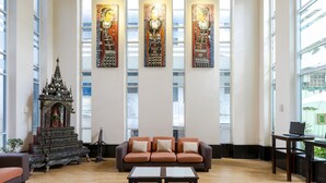A spacious room with a large window, a sofa, a small table, and a decorative altar. - Pinnacle Lumpini Park Hotel (Bangkok)