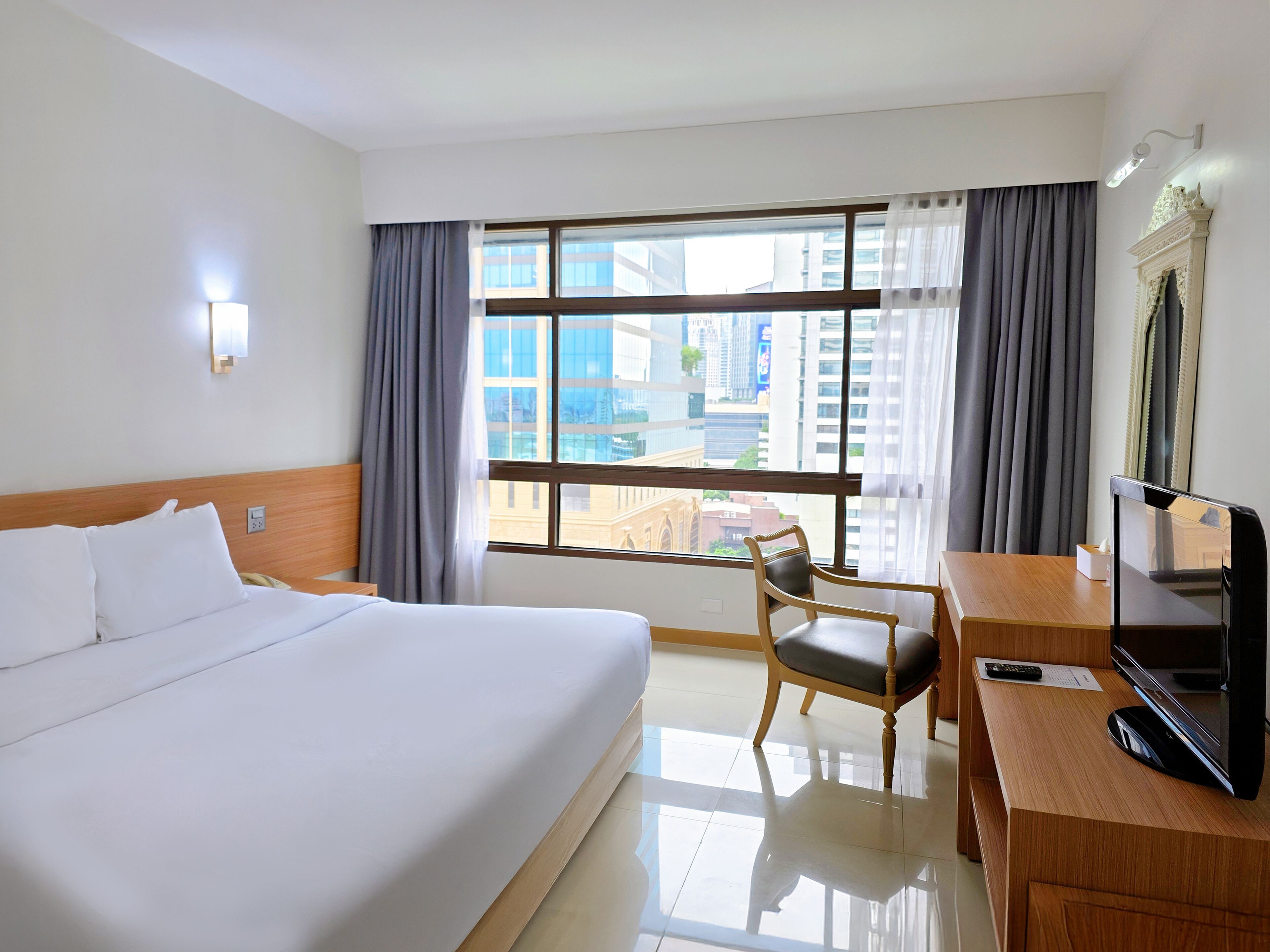 Habitación de hotel con una cama grande, un escritorio con televisor, una silla y una ventana con cortinas.