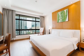 A hotel room with a large bed, a desk, a chair, a nightstand, and a window with a city view.