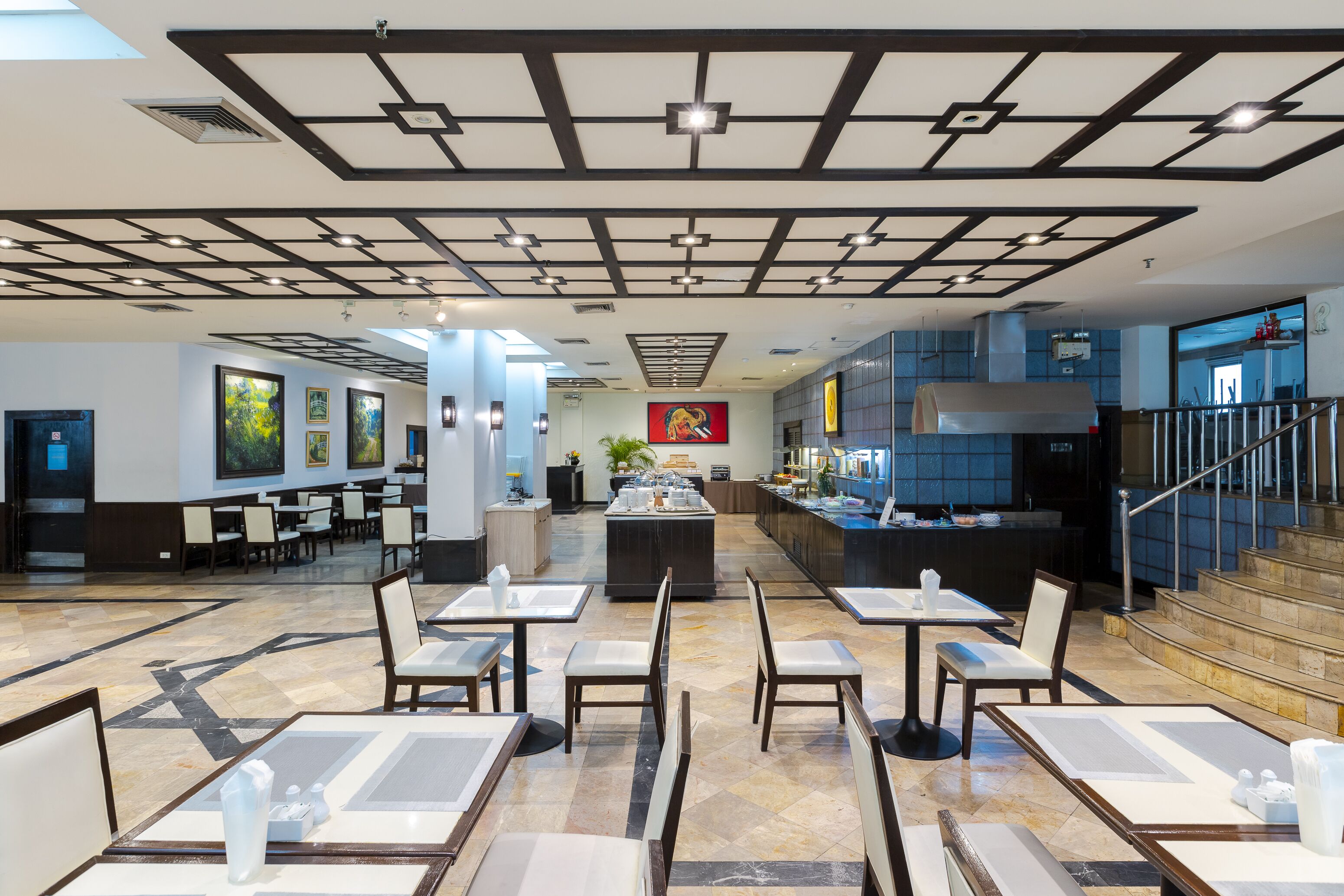 A modern restaurant with a central island, multiple seating areas, and a staircase leading to an upper level.
