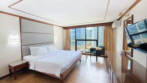 A hotel room with a large bed, a desk, a chair, a TV, and a window with a city view. - Pinnacle Lumpini Park Hotel (Bangkok)