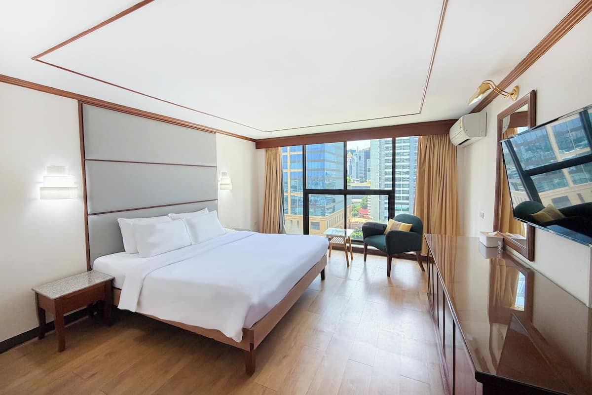 A hotel room with a large bed, a desk, a chair, a TV, and a window with a city view.