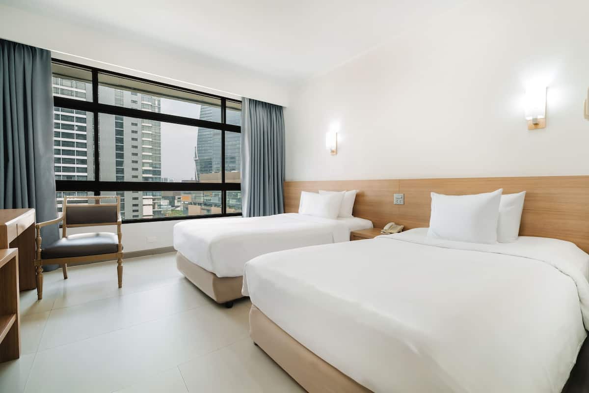 A hotel room with two beds, a desk, a chair, and a large window with curtains.