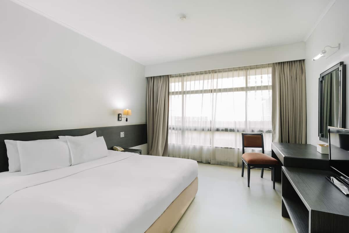 A hotel room with a bed, a desk, a chair, a television, and a window with curtains.