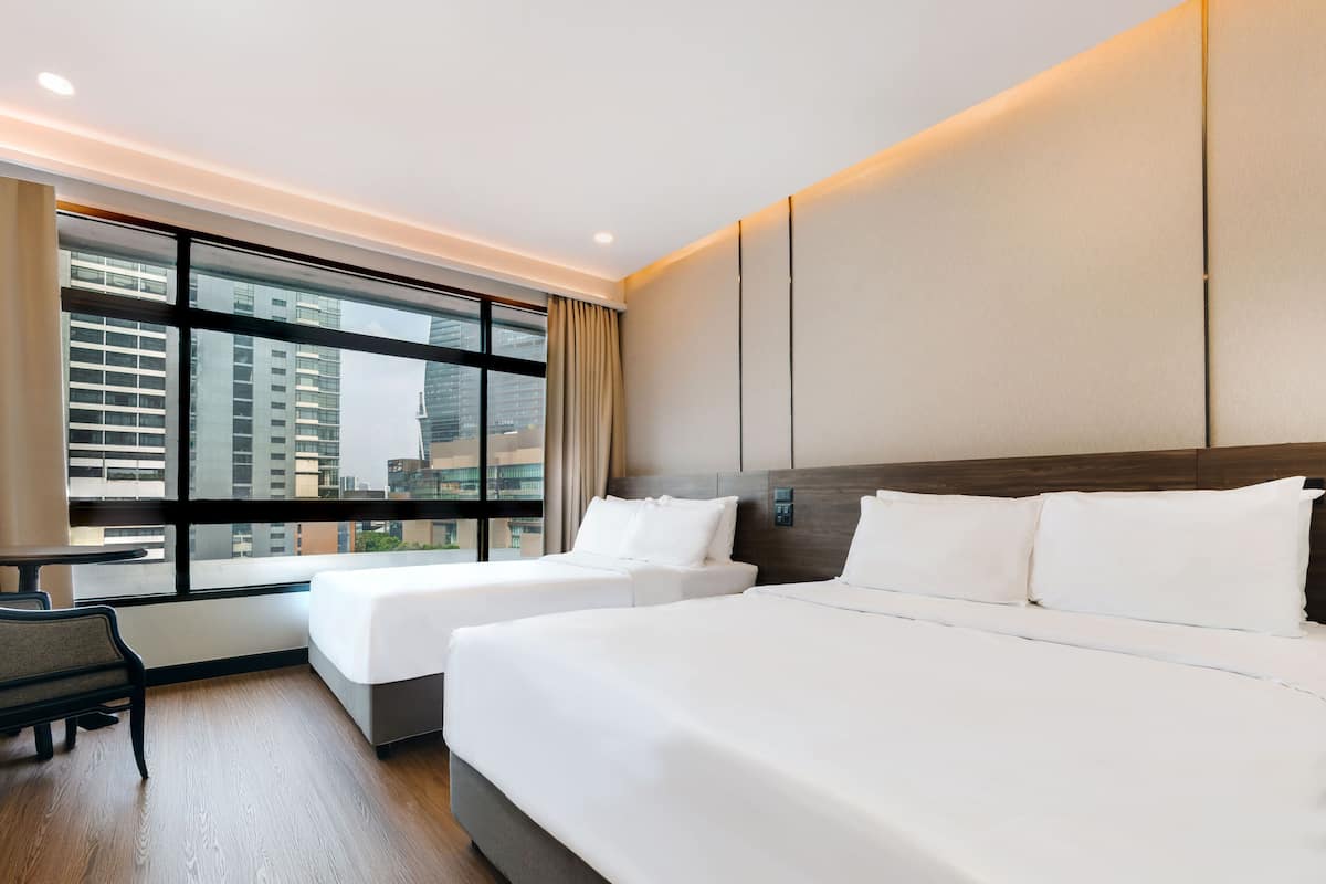A hotel room with two beds, a desk, and a large window with a city view.