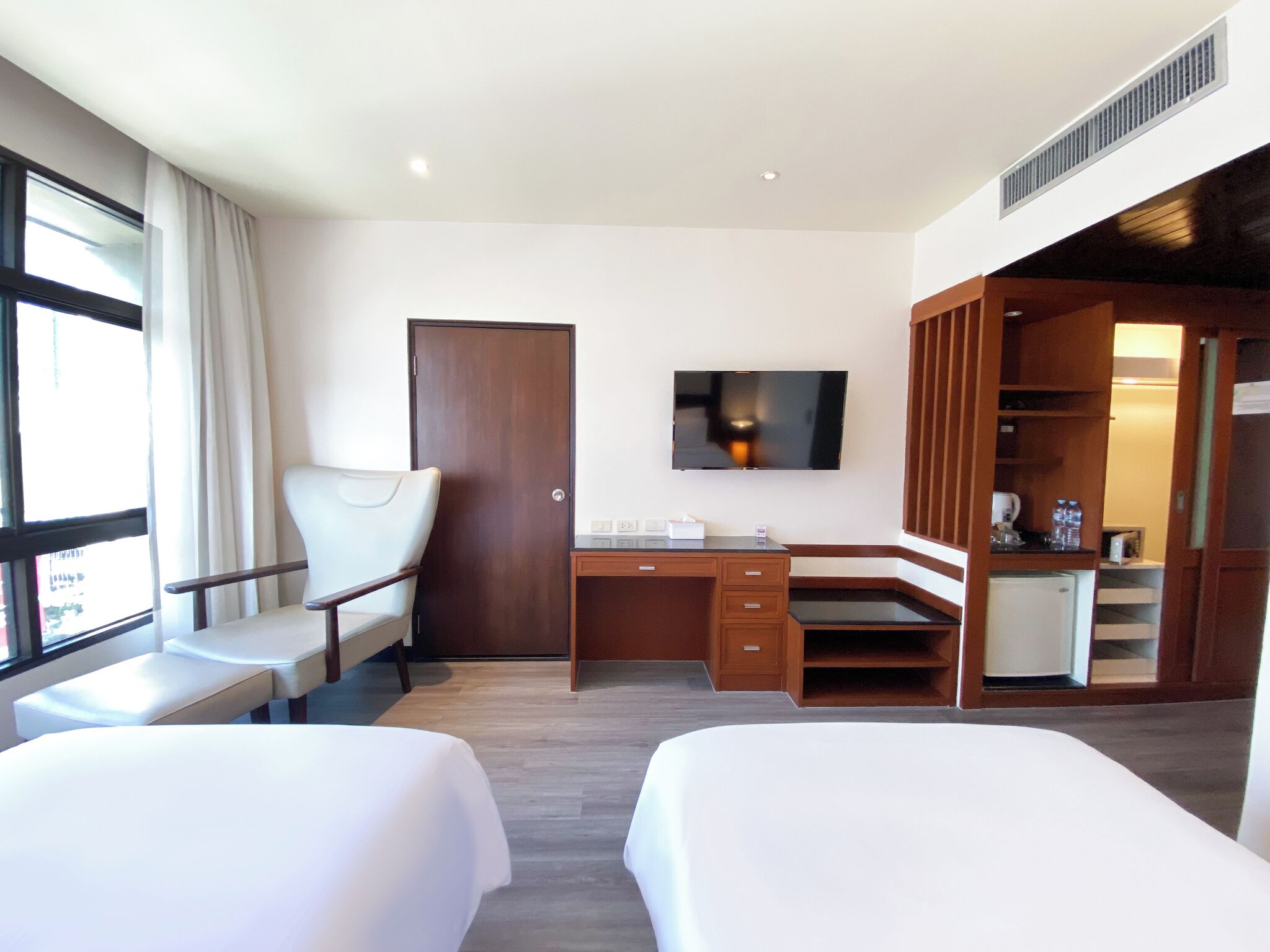 A hotel room with two beds, a desk, a chair, a TV, and a kitchenette.