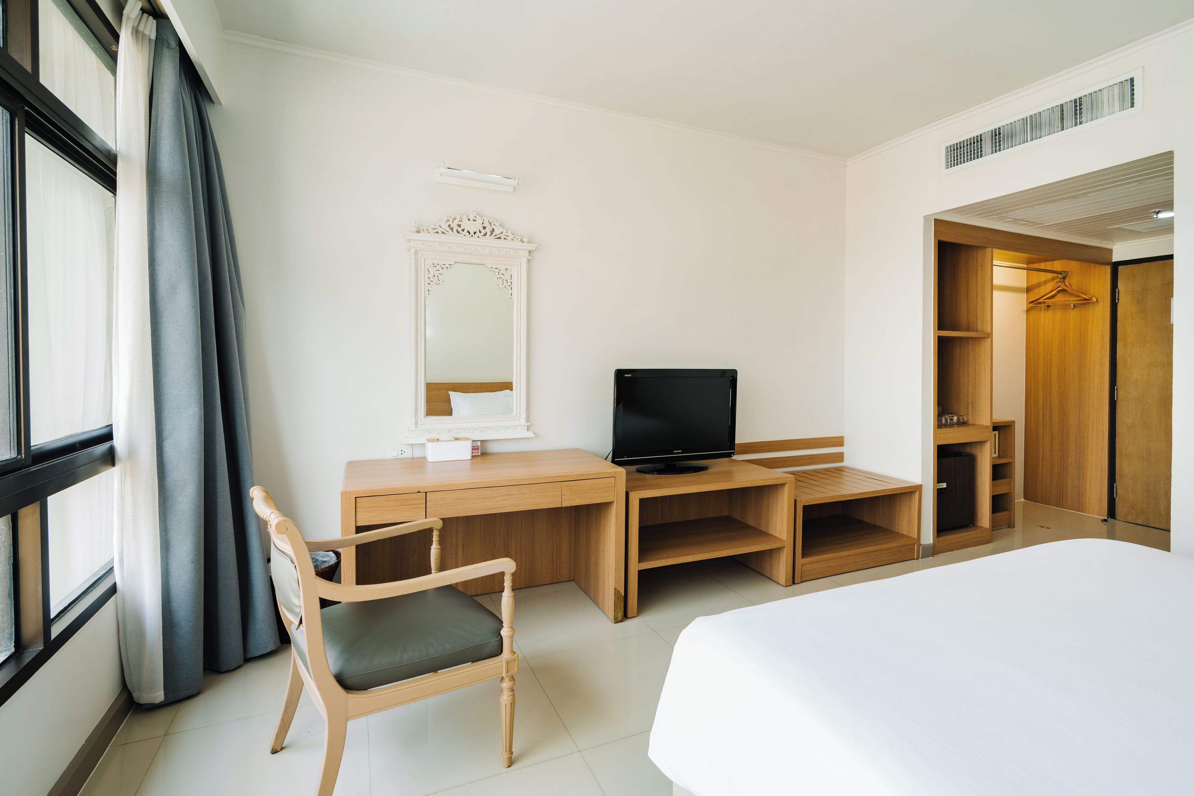 A hotel room with a bed, a desk with a TV, a chair, a wardrobe, and a mirror.