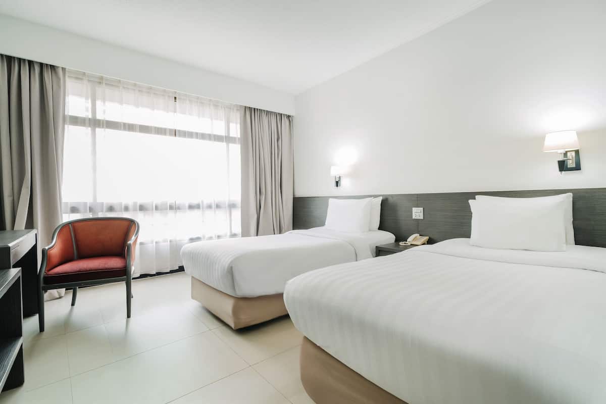 A hotel room with two beds, a desk, a chair, a lamp, and a window with curtains.