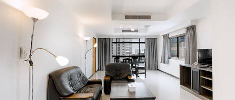 A modern living room with a sofa, a coffee table, a TV stand, and a dining area.