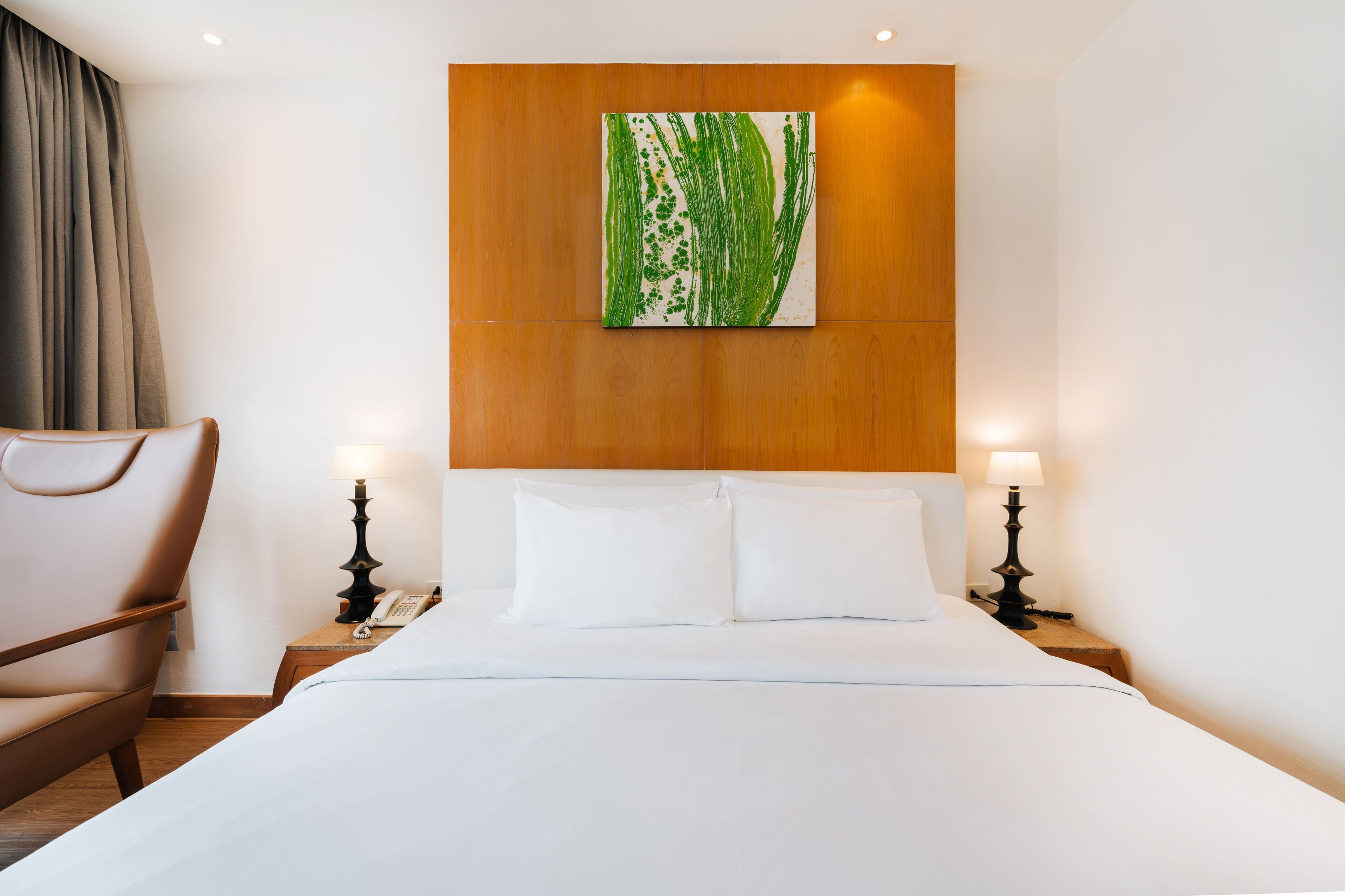 Une chambre d’hôtel avec un lit, deux tables de chevet avec des lampes, une chaise et un tableau au mur.