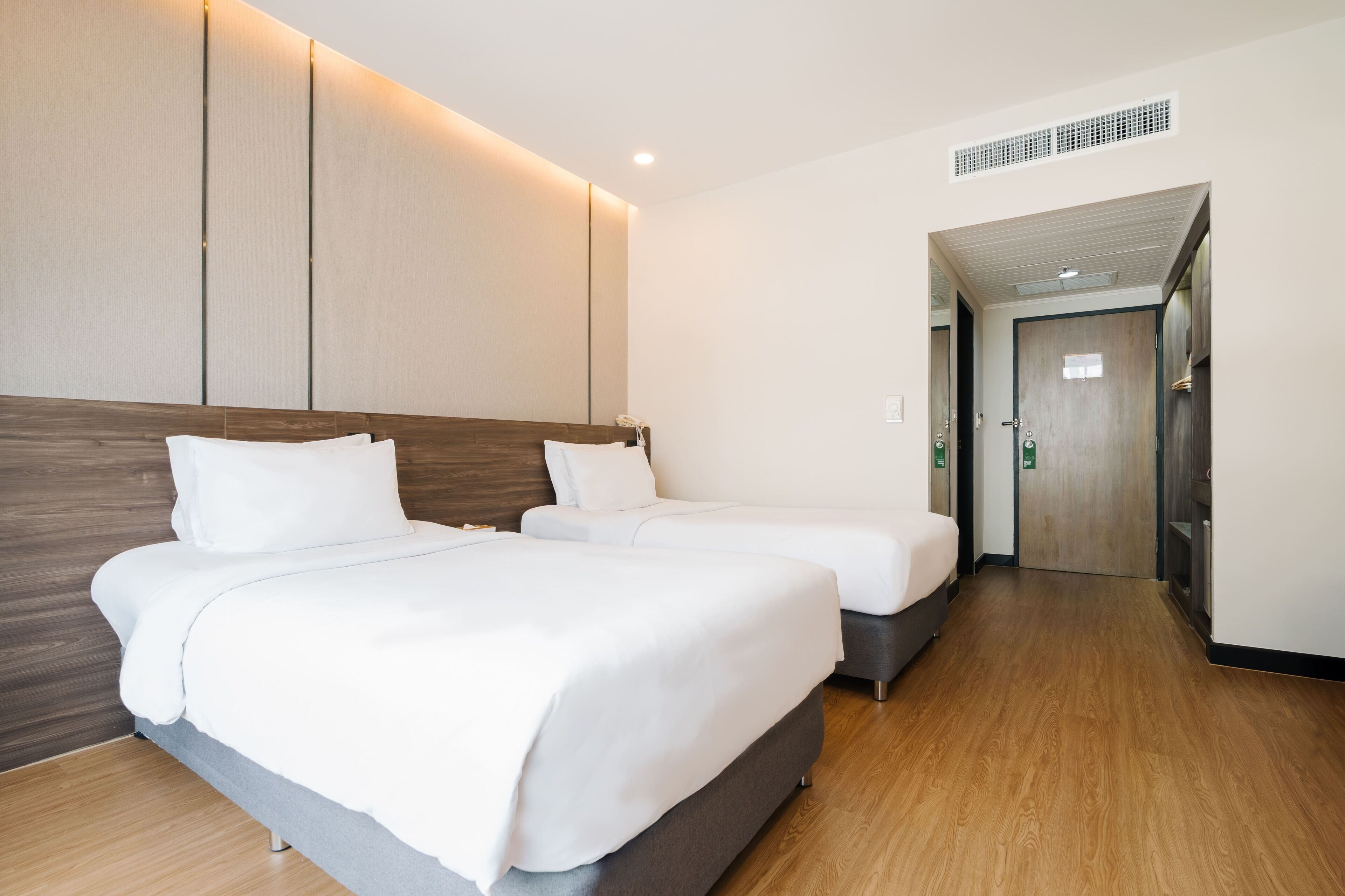 Habitación de hotel con dos camas, suelo de madera, diseño moderno y una puerta que da a otra habitación.