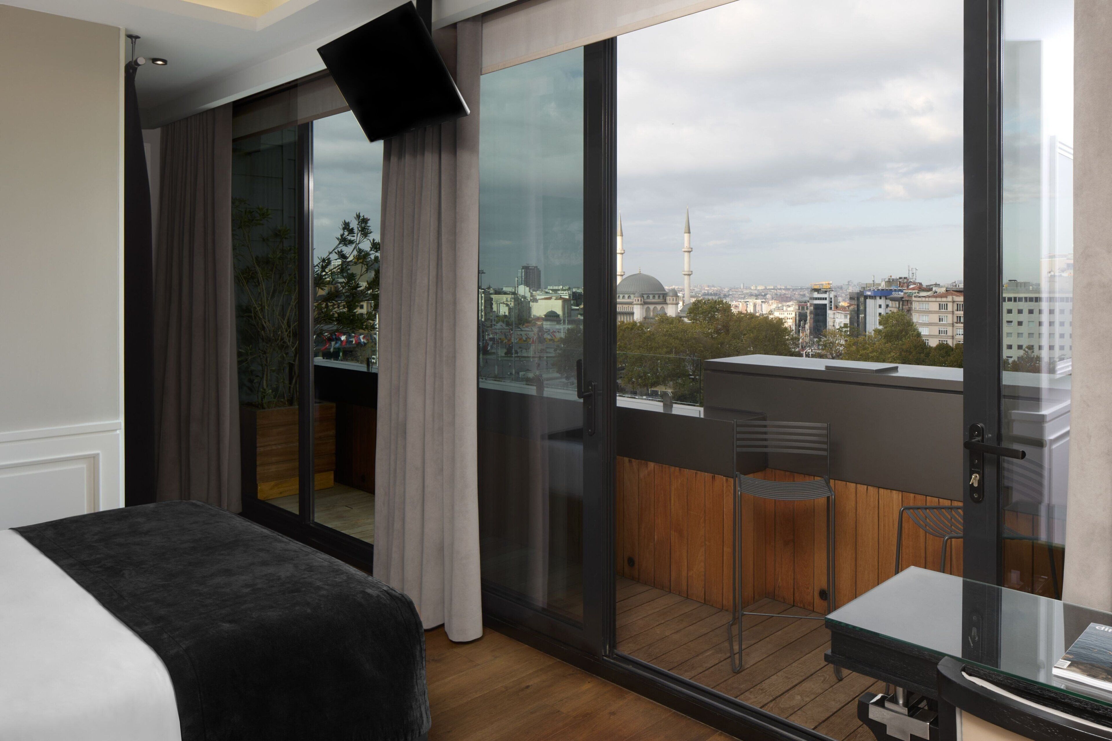 A modern hotel room with a large sliding glass door leading to a balcony with a city view.