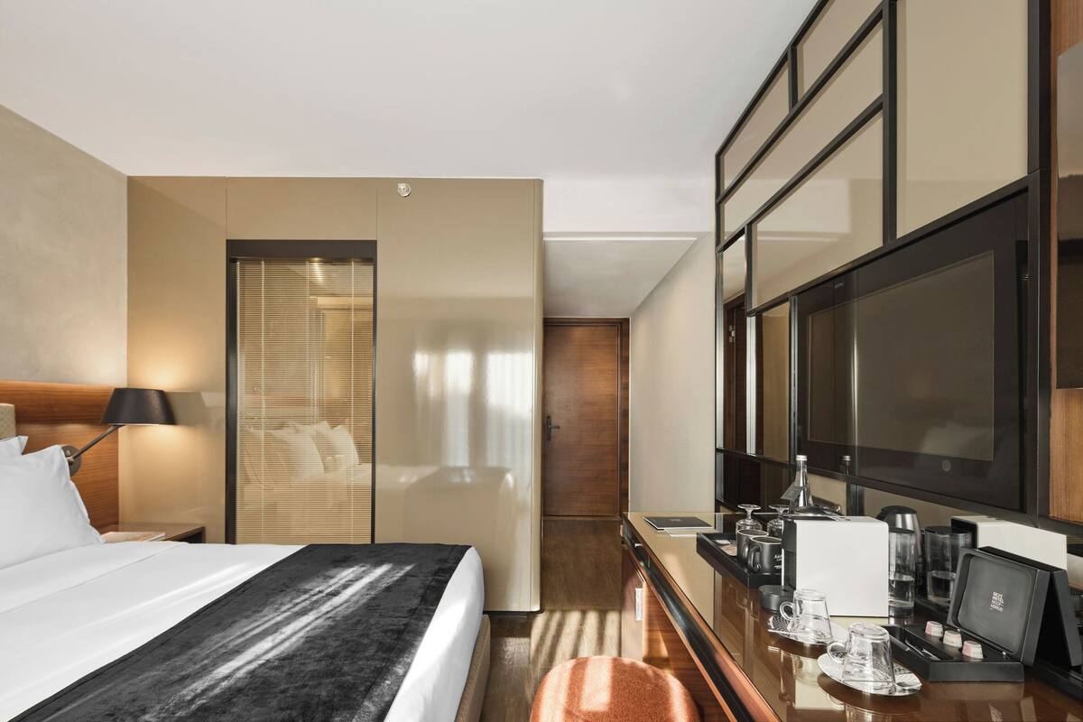 A hotel room with a bed, bedside table, lamp, and a minibar.
