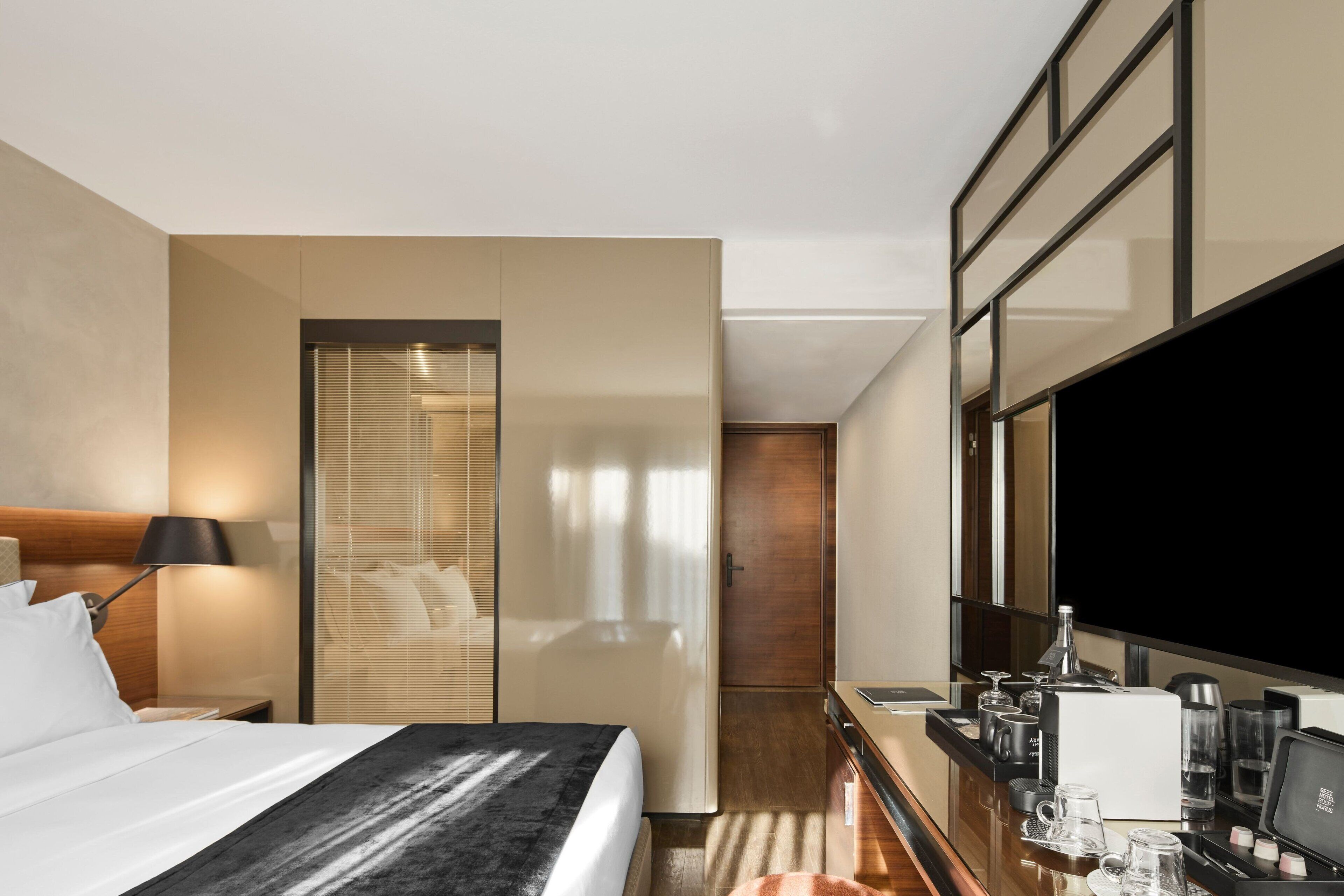 Et hotelværelse med seng, sengebord, lampe, fjernsyn og minibar.