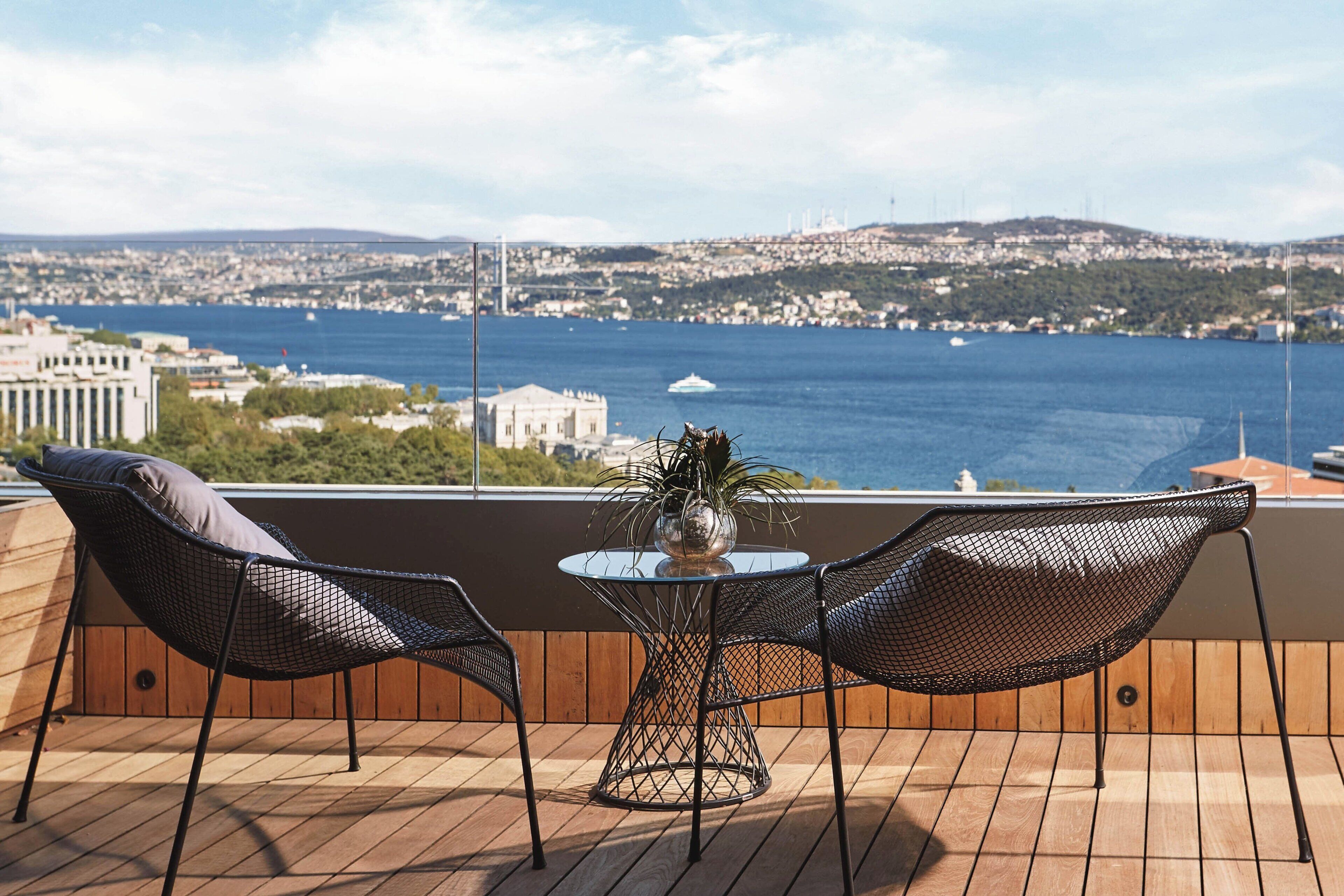 A balcony with two mesh chairs, a glass table, and a potted plant.