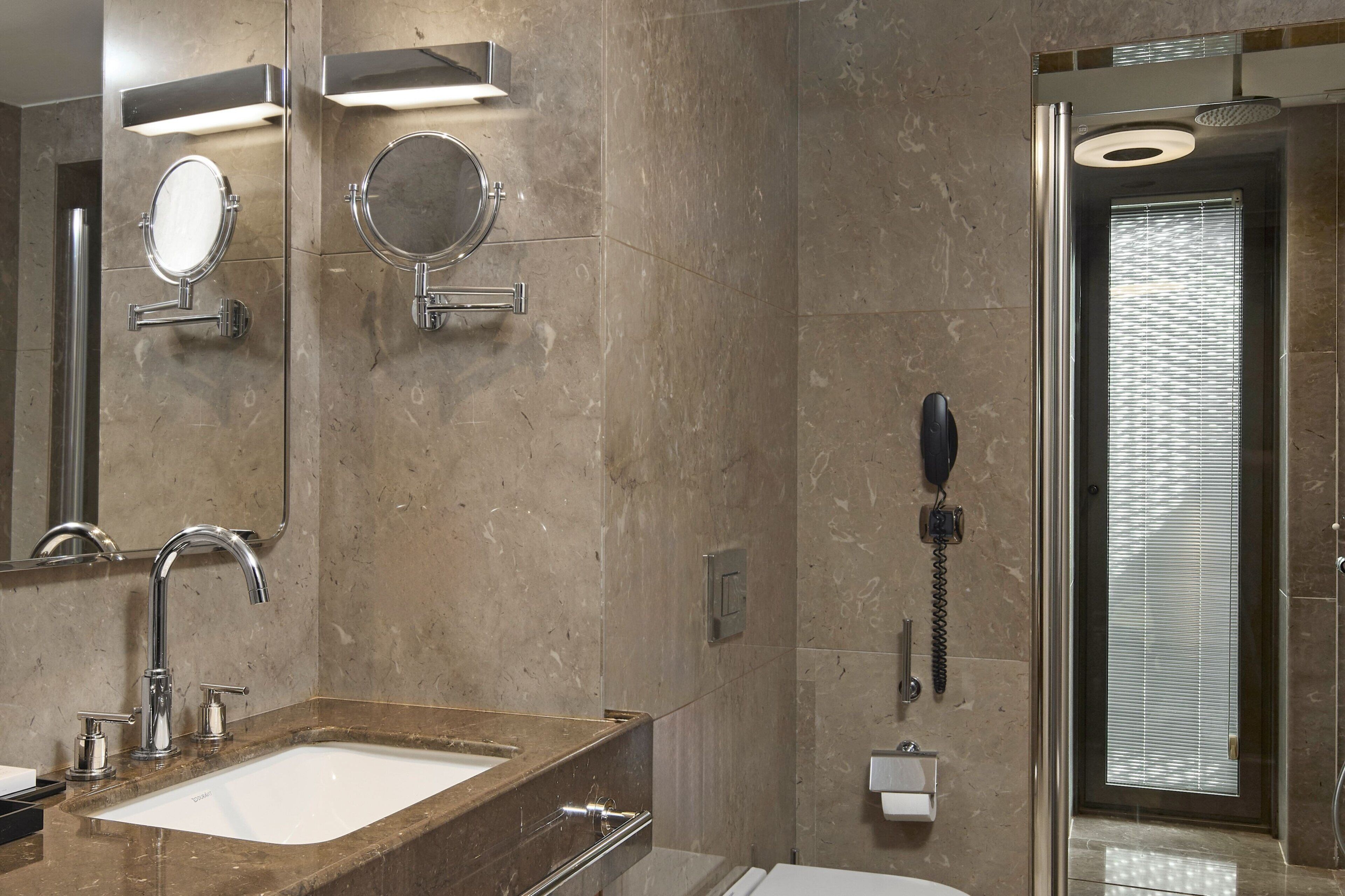 Un baño moderno con un lavamanos de mármol, dos espejos adosados a la pared, un cabezal de ducha de mano y un teléfono integrado.