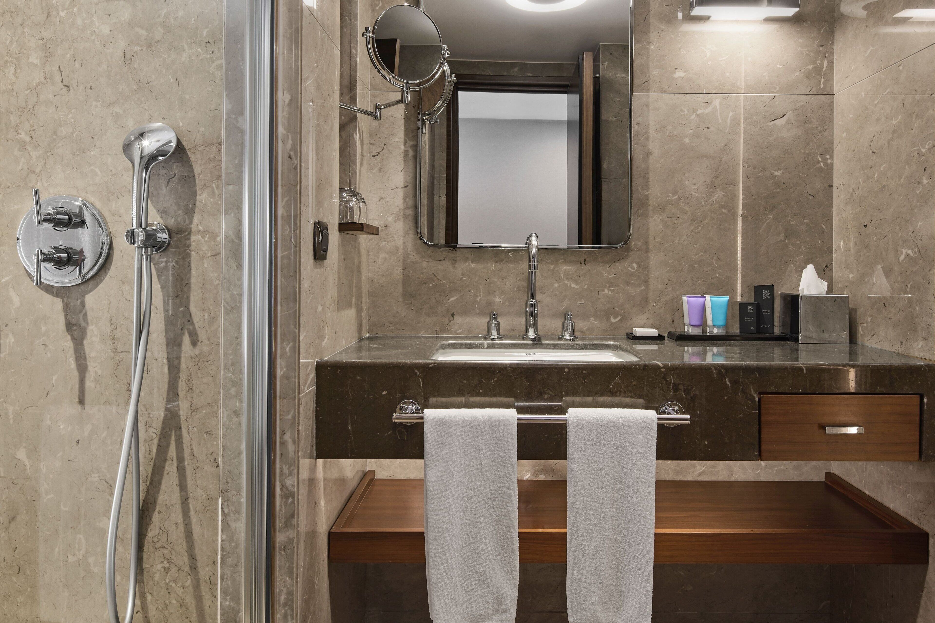 Un baño moderno con cabina de ducha de vidrio, un espejo grande, un lavabo con tocador y un perchero para toallas.