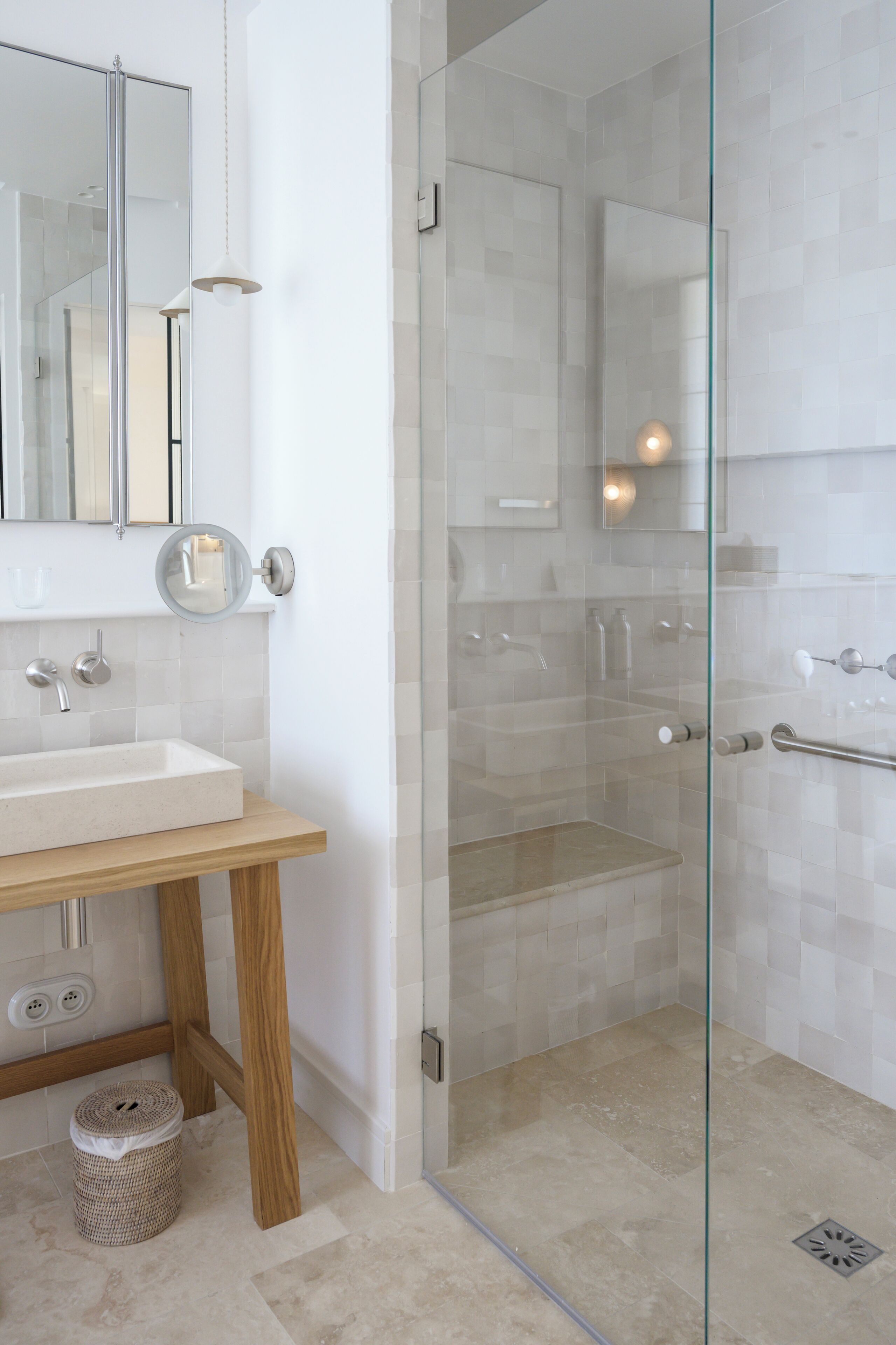 A modern bathroom with a glass-enclosed shower, a wooden vanity, and a round mirror.