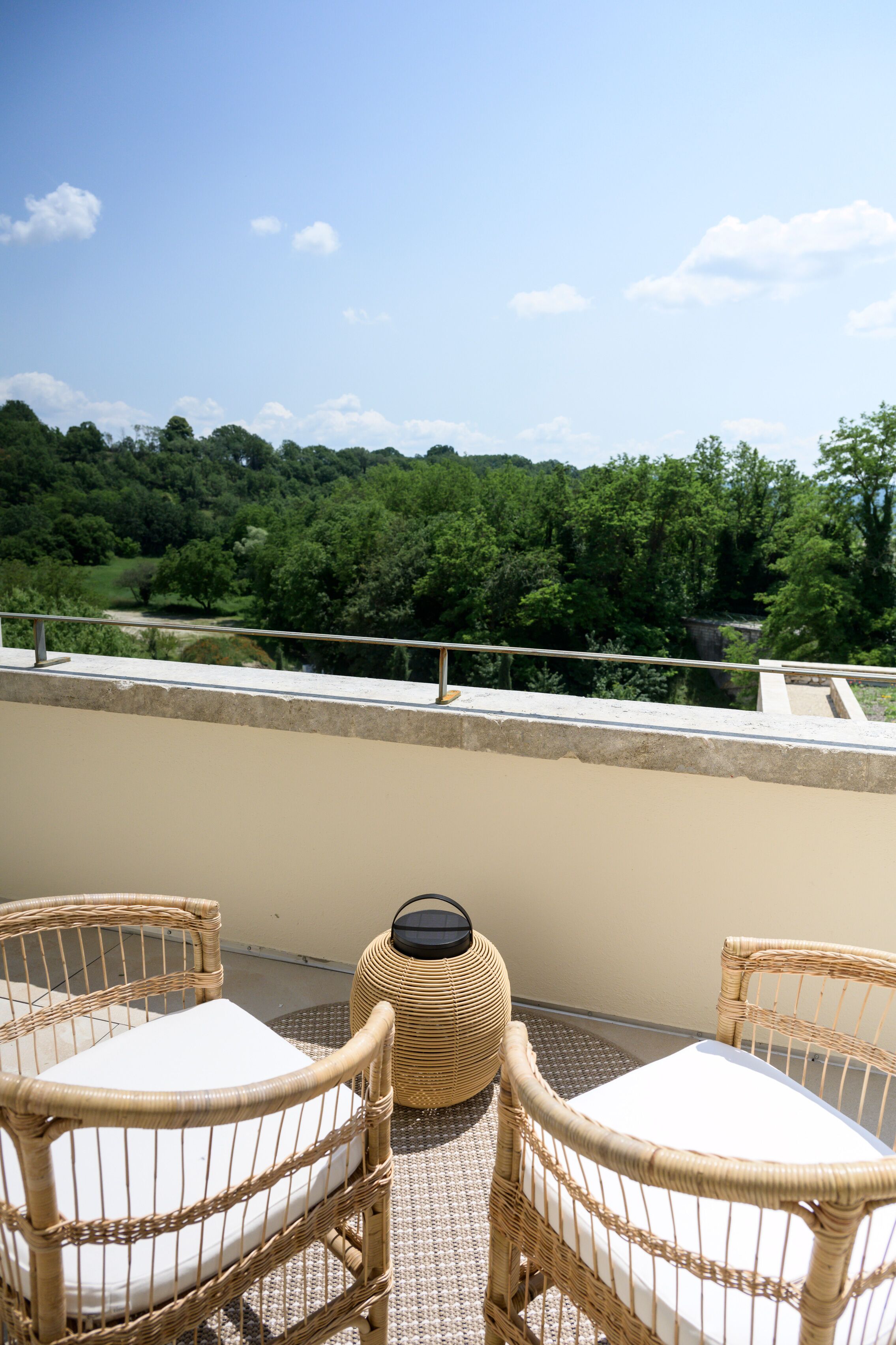 Un balcon doté de meubles en osier et offrant une vue sur une zone boisée.