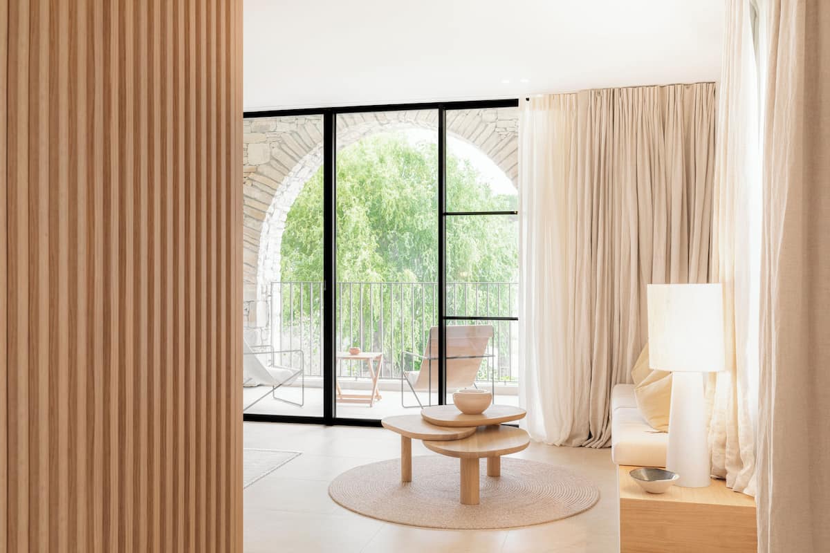 Una habitación moderna con un ventanal grande, una mesa redonda de madera, un sofá y una lámpara.