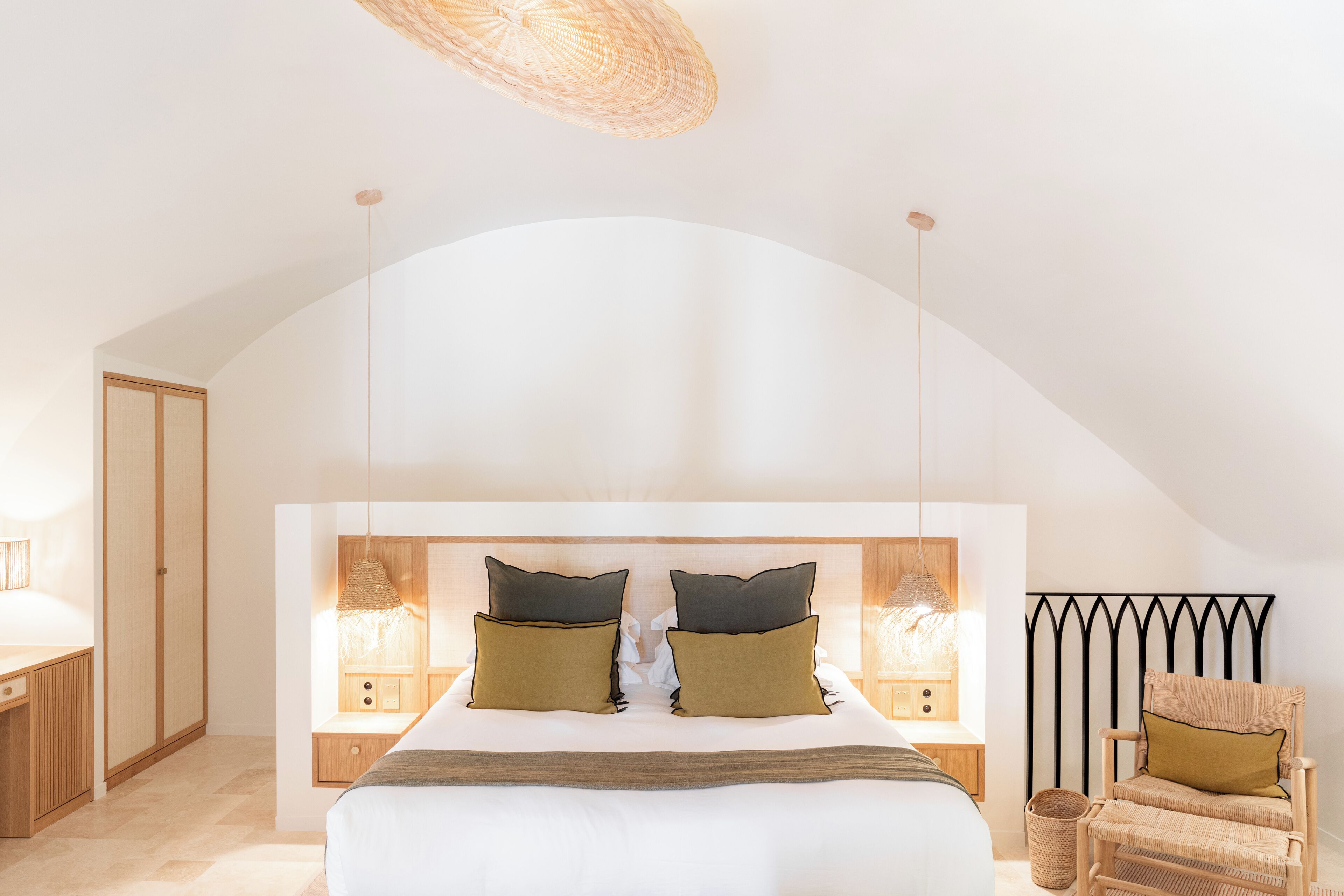 A bedroom with a large bed, bedside tables, a chair, and a unique arched ceiling.