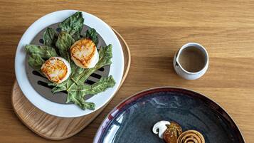 Uma mesa de madeira com dois pratos de comida, um com vieiras e vegetais, e outro com um prato escuro e um item em espiral.