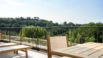 A balcony with wooden furniture and a metal railing overlooking a forested area.