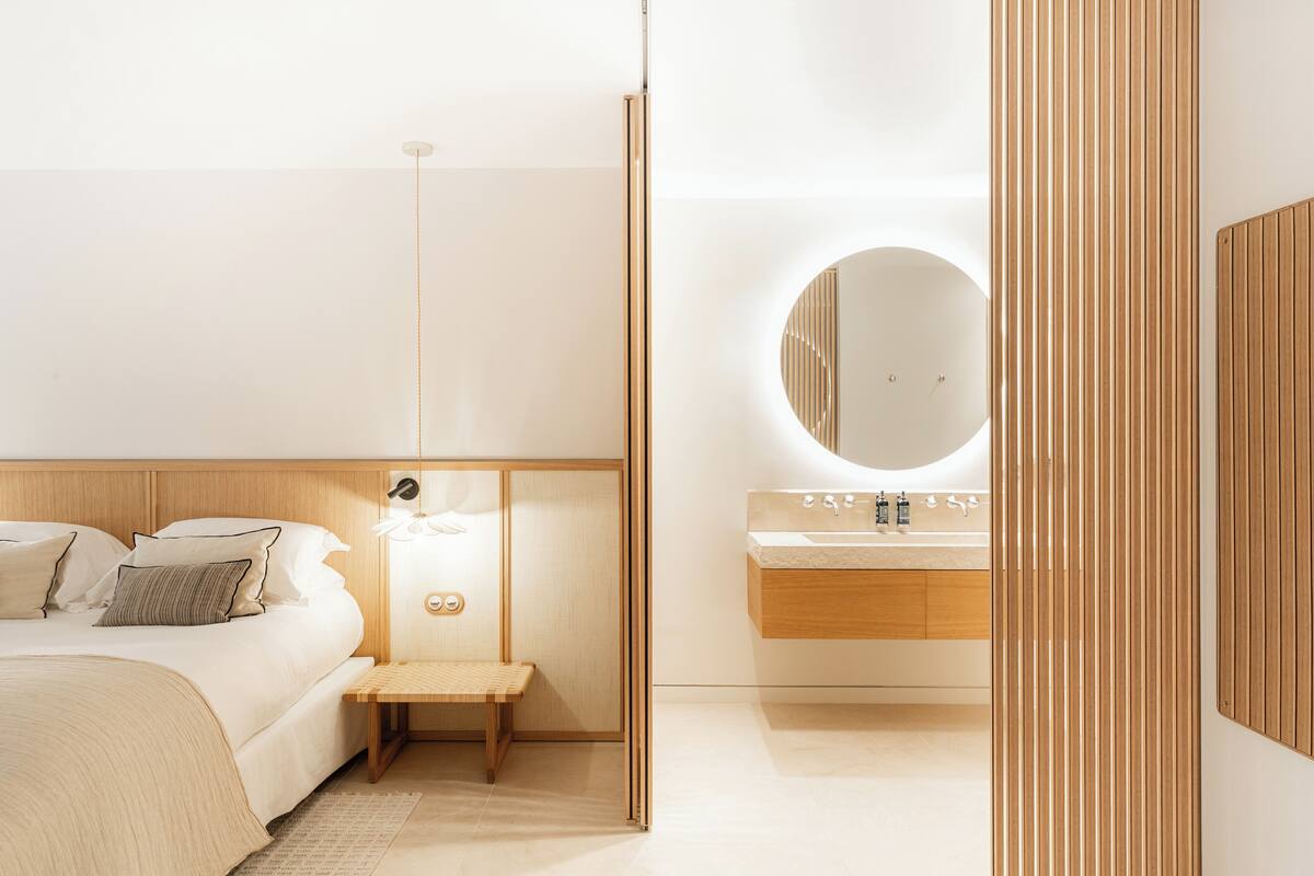Un dormitorio moderno con cama, mesita de noche y un espejo redondo sobre el lavabo.