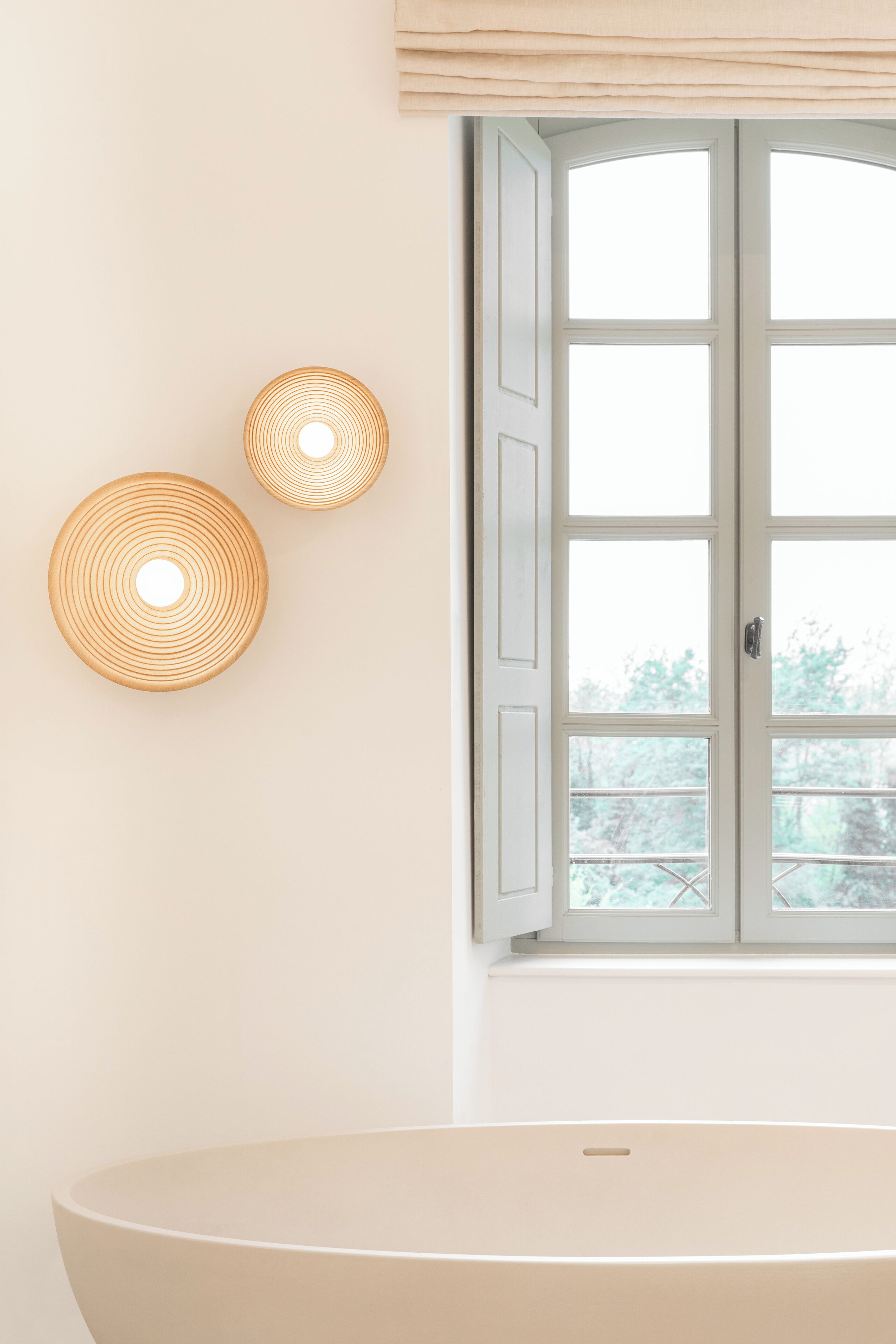 A bathroom with a bathtub, a window with curtains, and two wall-mounted light fixtures.