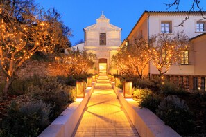 A pathway leading to a church with a bell tower, surrounded by trees and illuminated by warm lights. - Le Couvent des Minimes, Un Hôtel & Spa L'Occitane en Provence (Mane)