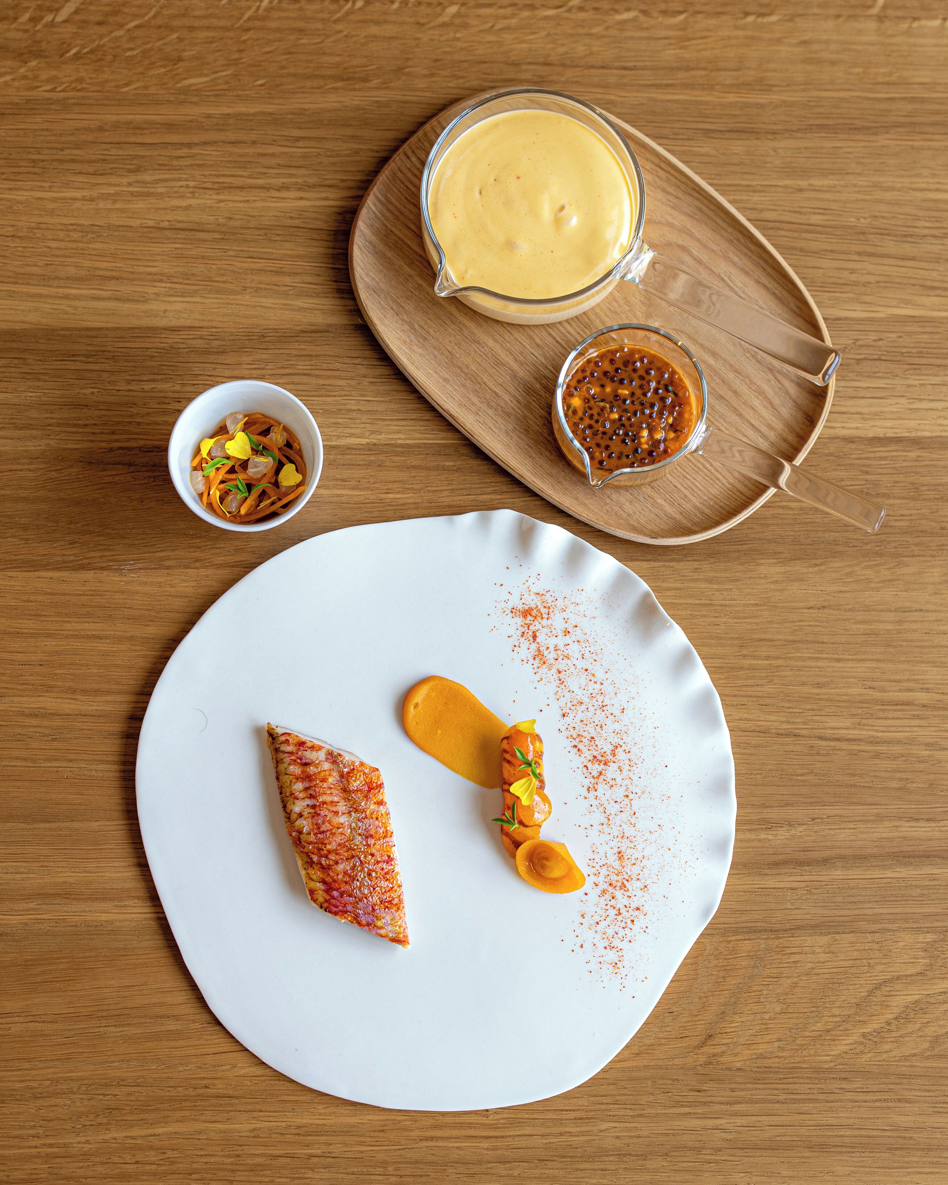 A white plate with a slice of pizza and a mango slice on a wooden table.