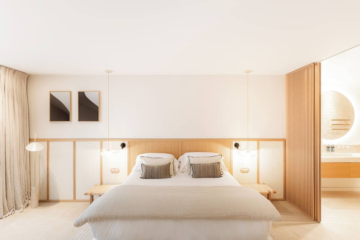 Un dormitorio moderno con una cama grande, mesitas de noche, cabecera de madera, un espejo montado en la pared y una lámpara de noche.