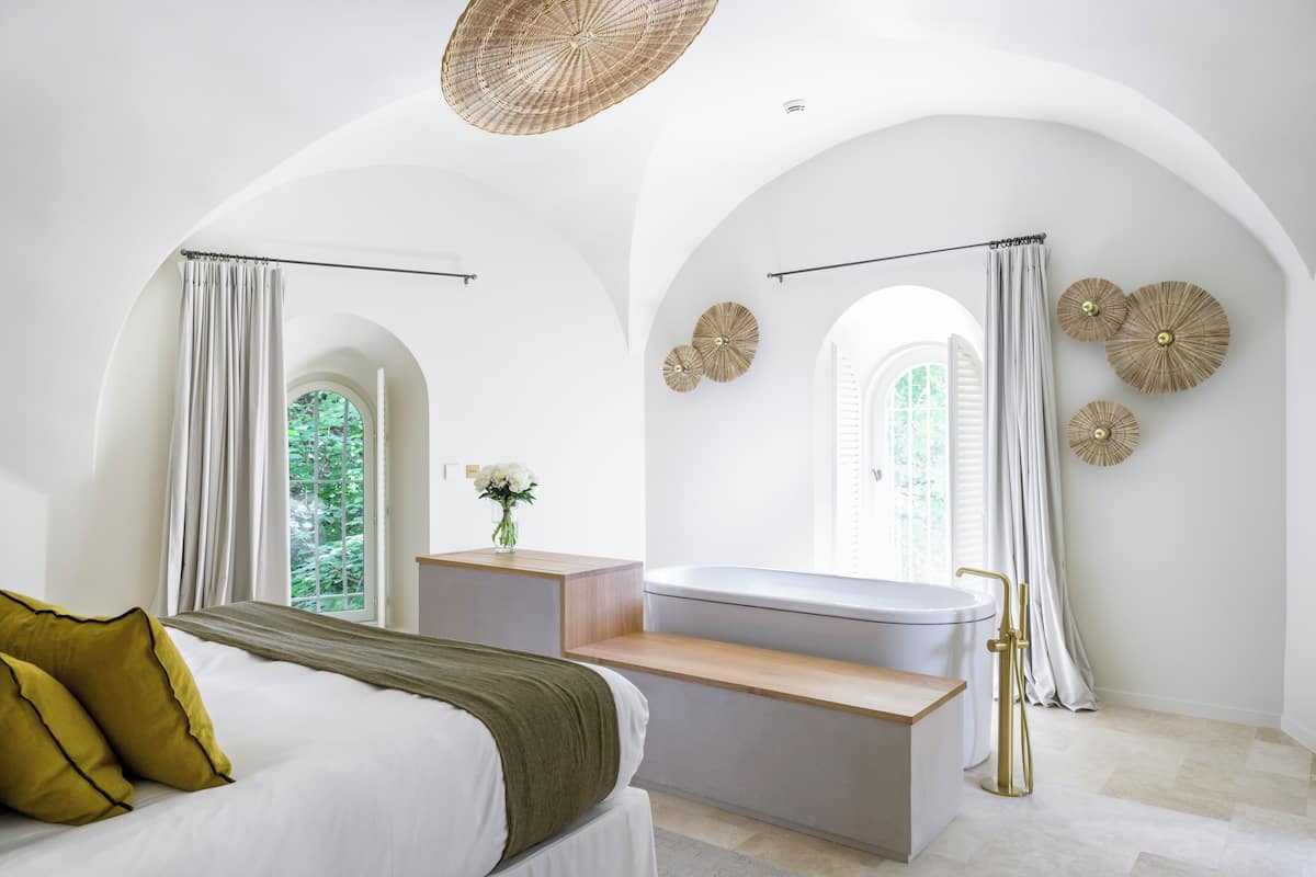 Un dormitorio moderno con cama, tocador, bañera y ventana con cortinas.