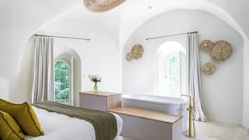 A modern bedroom with a bed, a vanity, a bathtub, and a window with curtains.