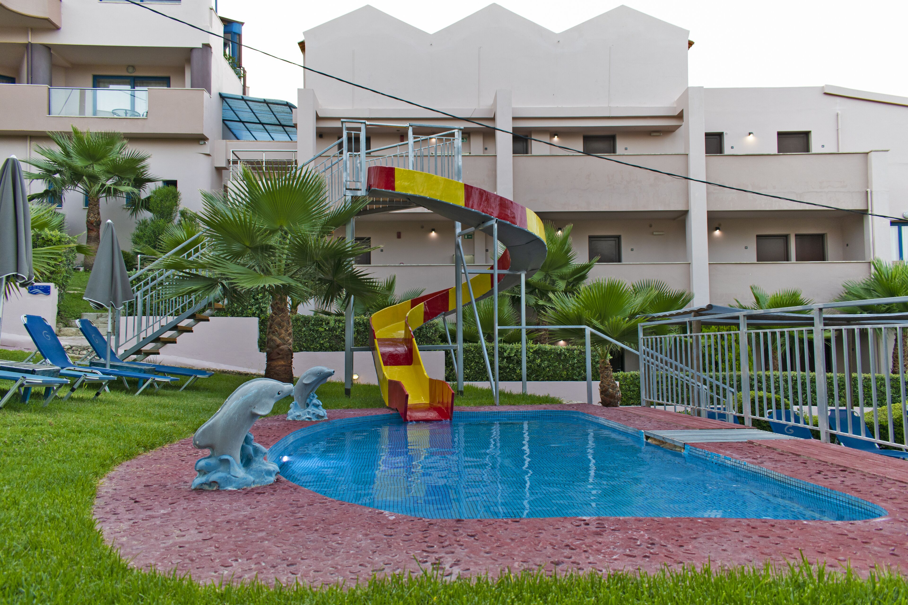 Una piscina con un tobogán colorido, sillas de descanso y palmeras.