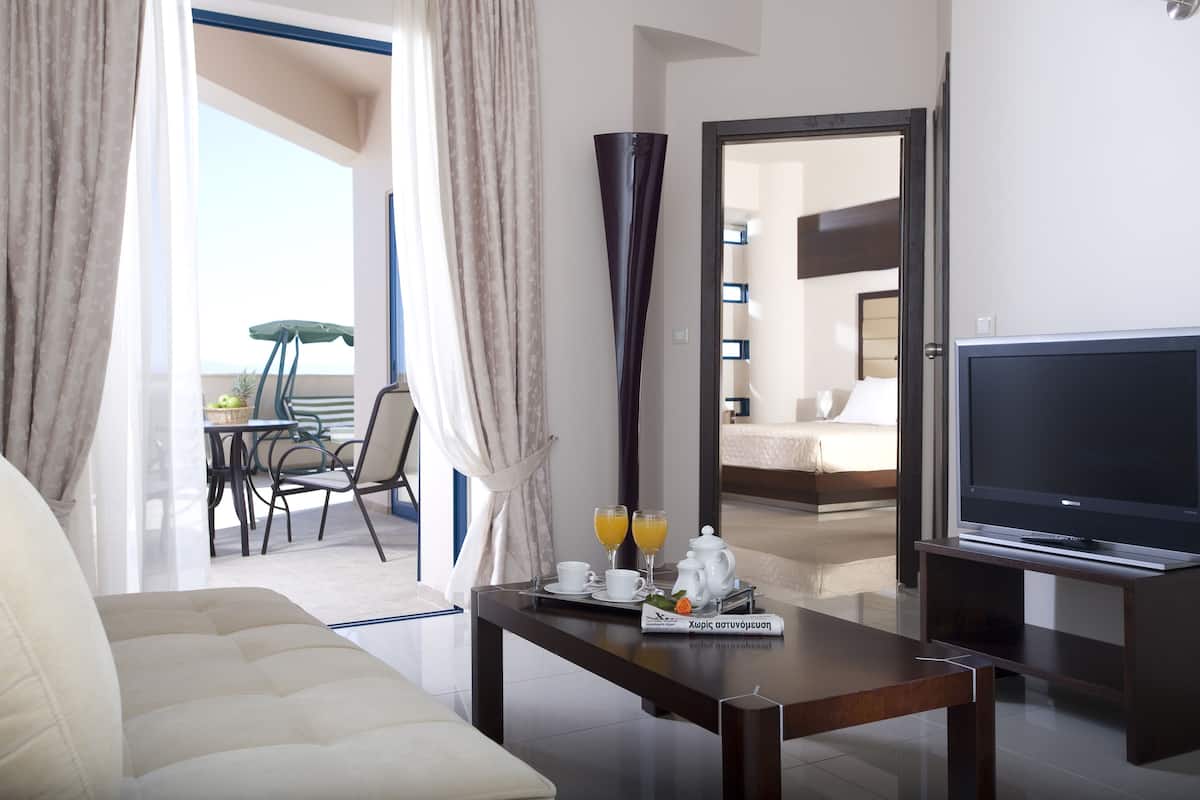 Habitació d'hotel amb un sofà, una taula de cafè amb un plat de suc d'aranja i una teiera, una televisió i un balcó amb taula i cadires.