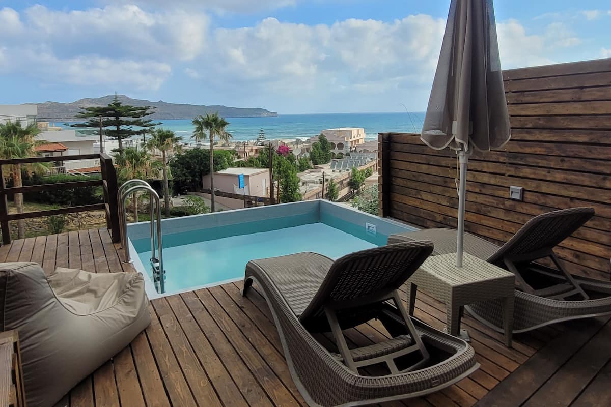 Una terrassa de fusta amb una piscina, gandules i vista a l'oceà i els edificis.