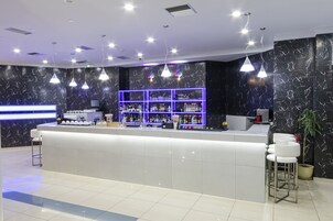 Un área de bar moderna con una pared de mármol, una estantería iluminada con neón y una barra blanca.