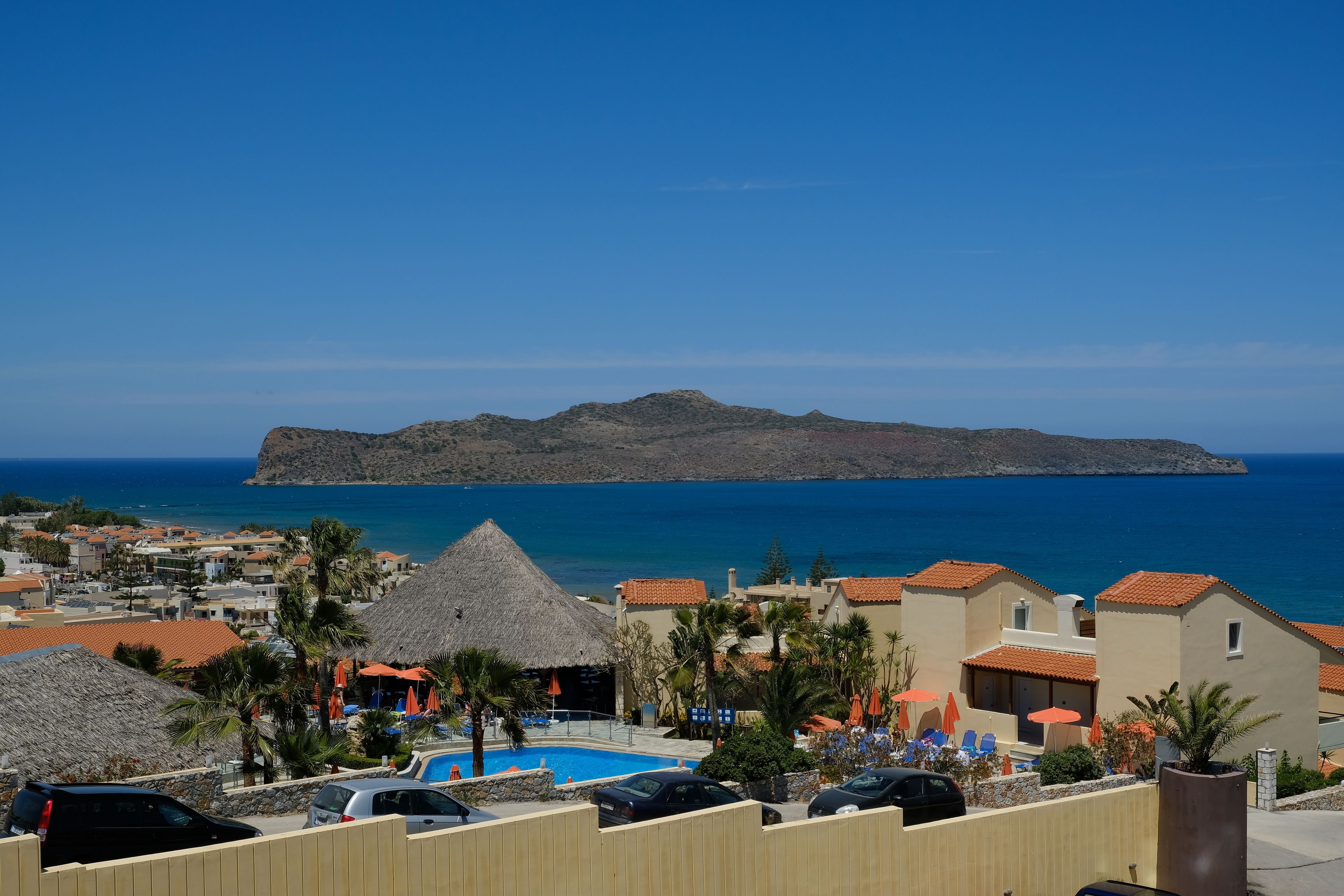 A resort with a swimming pool, beach umbrellas, and a view of the sea and distant island.