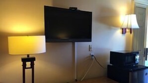 A hotel room with a flat-screen TV mounted on the wall, a bedside lamp, a coffee maker, and a small table with a clock. - Sands Motel (Riverside)