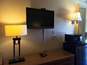 A room with a television mounted on the wall, a lamp on a table, and a microwave. - Sands Motel (Riverside)
