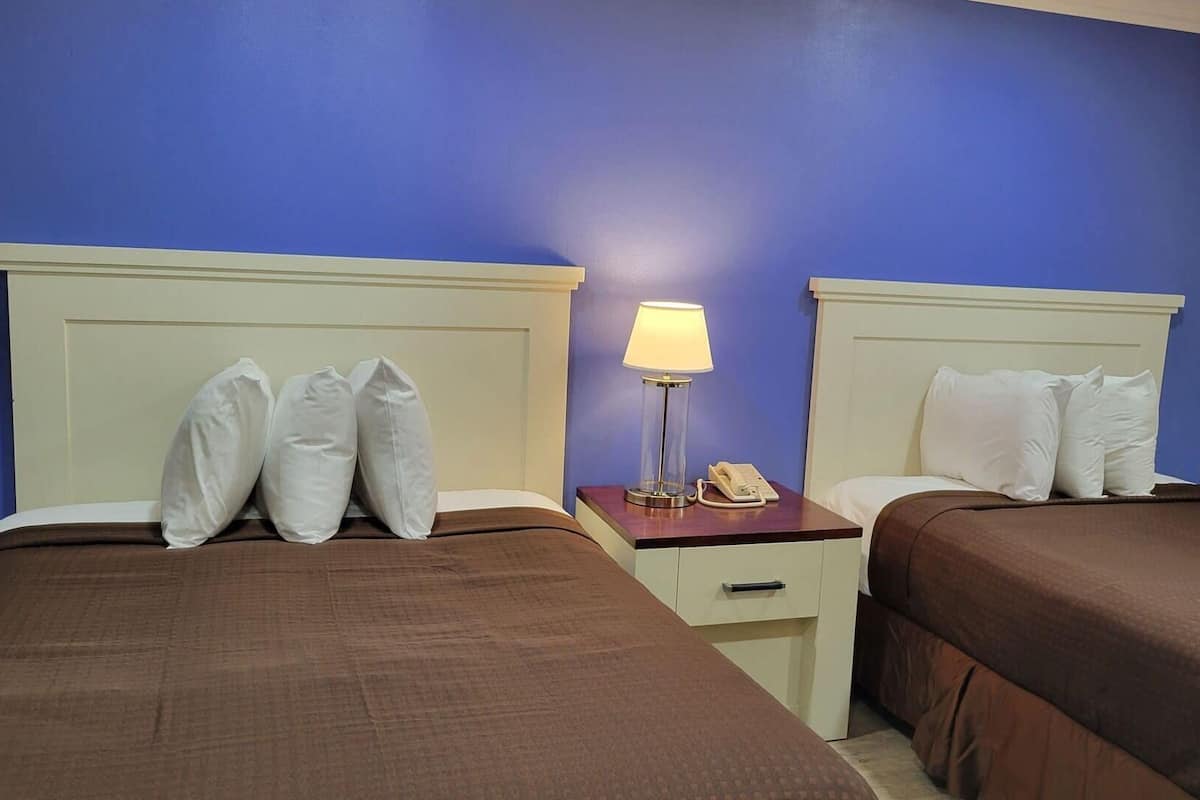 A hotel room with two beds, a nightstand with a lamp, and a phone.