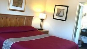 A hotel room with a large bed, a wooden headboard, a nightstand with a lamp, and two framed pictures on the wall. - Sands Motel (Riverside)