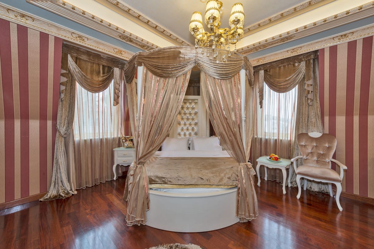 A luxurious bedroom with a four-poster bed, a chandelier, and striped wallpaper.