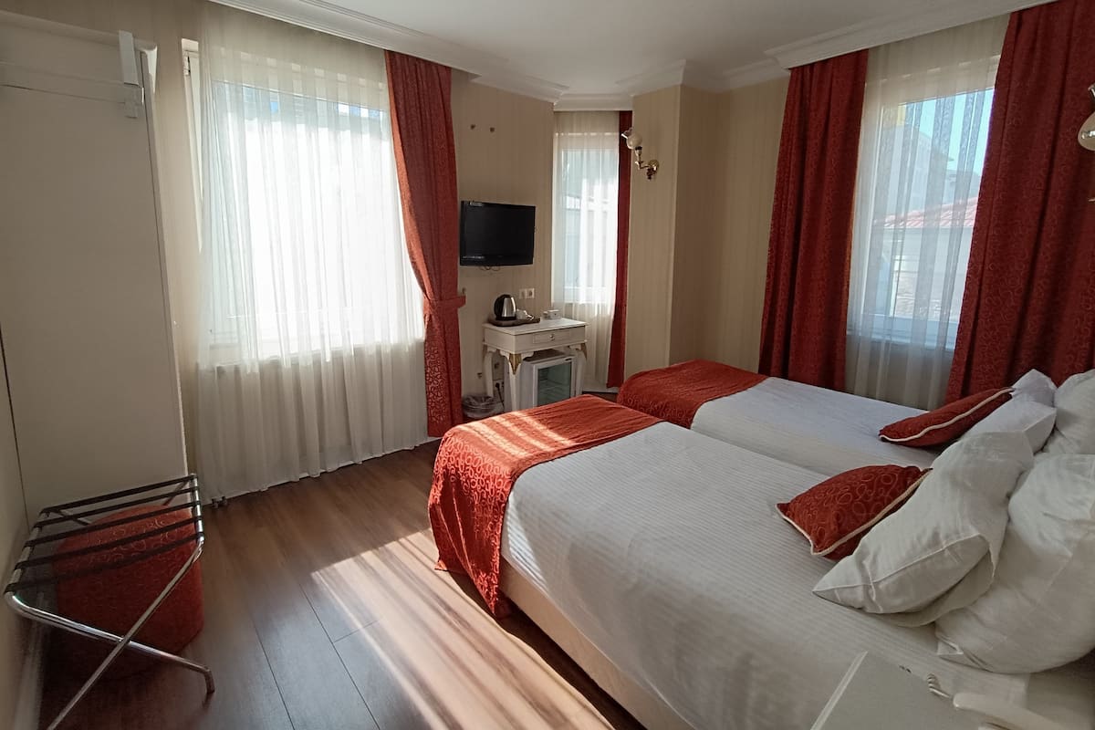 A hotel room with two beds, a desk with a television, and a window with curtains.
