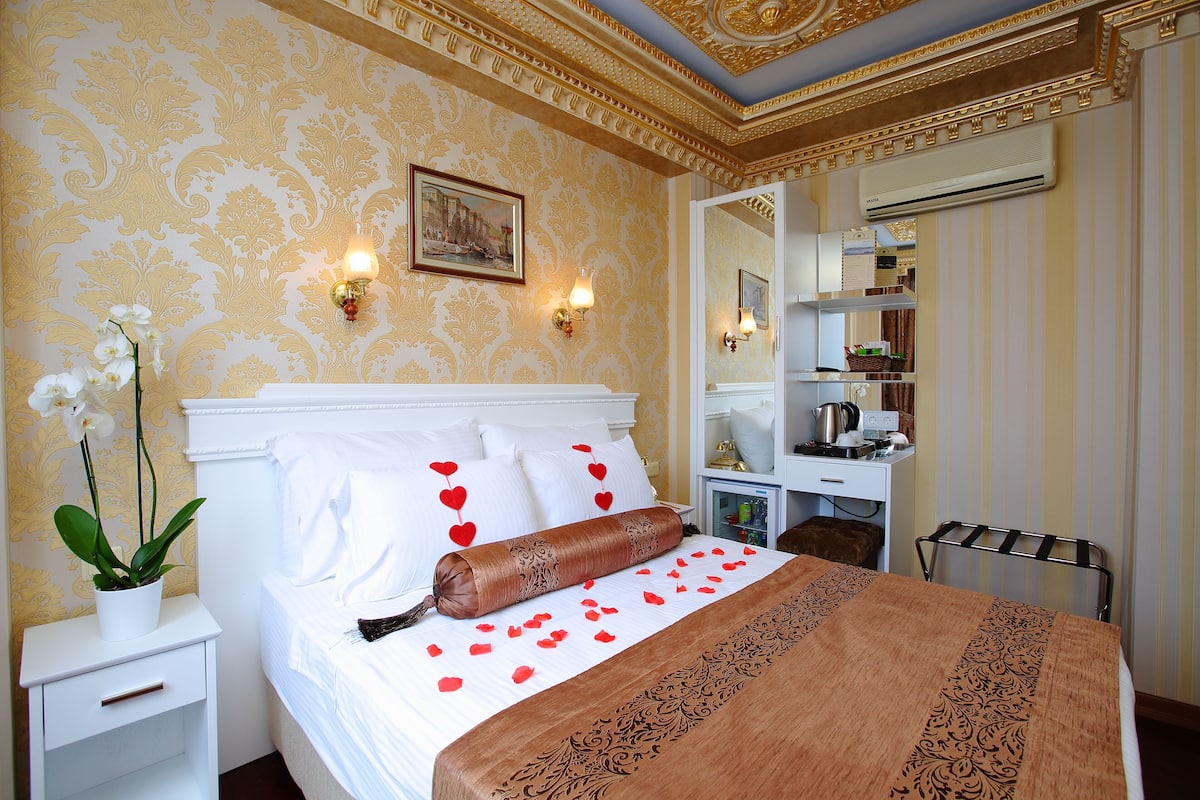 A hotel room with a bed, a nightstand, a potted plant, and a dresser with a mirror.