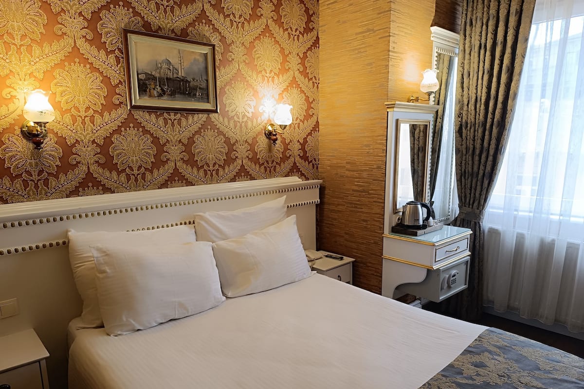 A hotel room with a large bed, two bedside lamps, a nightstand, a dresser, a mirror, and a window with curtains.