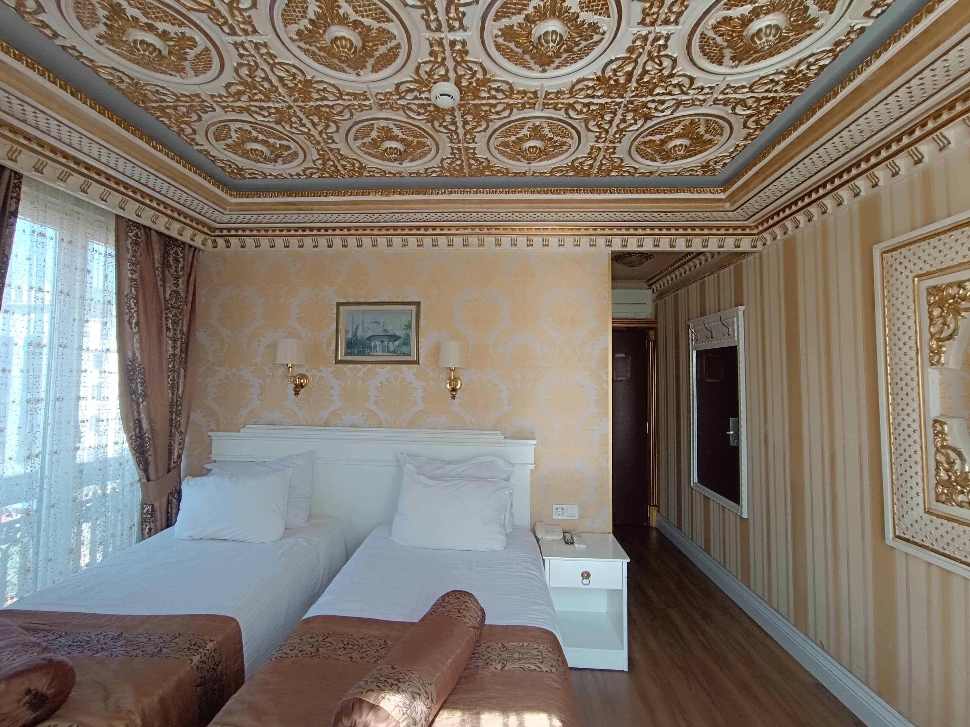 Habitación de hotel con una cama grande, dos mesitas de noche, un televisor de pared y detalles decorativos en el techo.