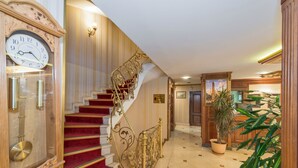 A grand staircase with red carpeted steps and ornate gold railings, leading to a well-lit hallway with a large clock and a potted plant. - Golden Horn Hotel - Special Class (Istanbul)