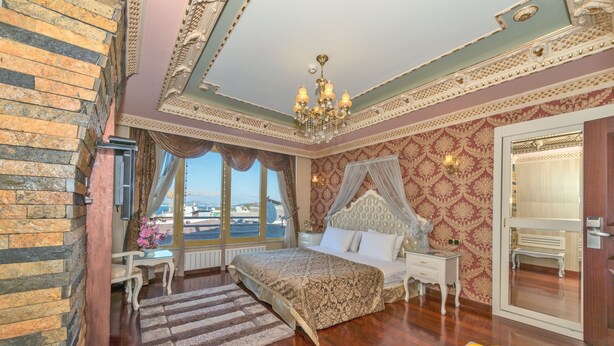 A bedroom with a large bed, a chandelier, a view of the city, and a fruit bowl on the nightstand. - Golden Horn Hotel - Special Class (Istanbul)